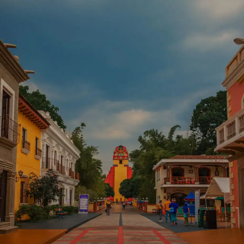 Calle en Tepoztlán con la Torre del Tepozteco al fondo, algunas personas caminando y edificios coloridos, ambiente tradicional y turístico en la región de Morelos, México. – SoyMigrante.com REVISTA