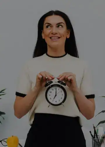 Reloj despertador en manos de joven mujer sonriente, concepto de gestión del tiempo y productividad en la comunidad migrante en España.