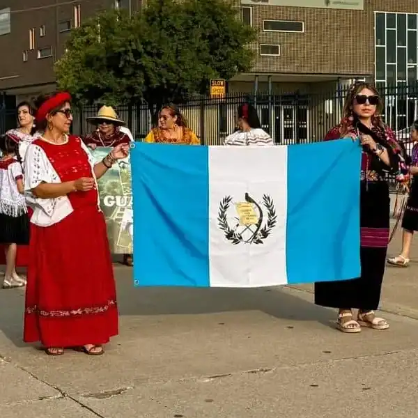 No éramos muchas pero sí todas guatemaltecas y con gran entusiasmo para representar a nuestro país con indumentarias indígenas, la bandera y cantos tradicionales. (Fotografía cortesía Kiara Vera) – SoyMigrante.com REVISTA Bandera de Guatemala en manifestación cultural en el extranjero, destacando la participación de inmigrantes guatemaltecos y el orgullo de la comunidad migrante en eventos internacionales.