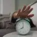 Despertador mint verde, mano tocando una alarma, en un entorno de oficina o dormitorio, enfoque en reloj, concepto de tiempo y productividad para artículos de inmigración y migrante.