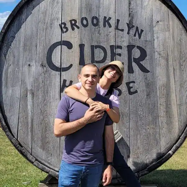 Amigos en un viñedo con barril de cerveza Brooklyn Cider House, disfrutando del enoturismo y la cultura cervecera artesanal, en un entorno rural y acogedor. – SoyMigrante.com REVISTA