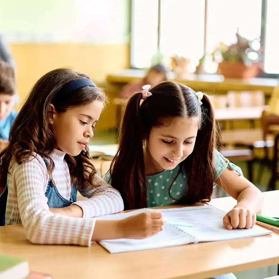 Estudiantes escolares en aula, leyendo y estudiando juntas en un ambiente educativo, promoviendo el aprendizaje y la inclusión en la comunidad escolar. – SoyMigrante.com REVISTA