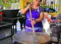 Artesana preparando comida en una feria cultural y gastronómica en un puesto callejero en un ambiente festivo y vibrante en México.