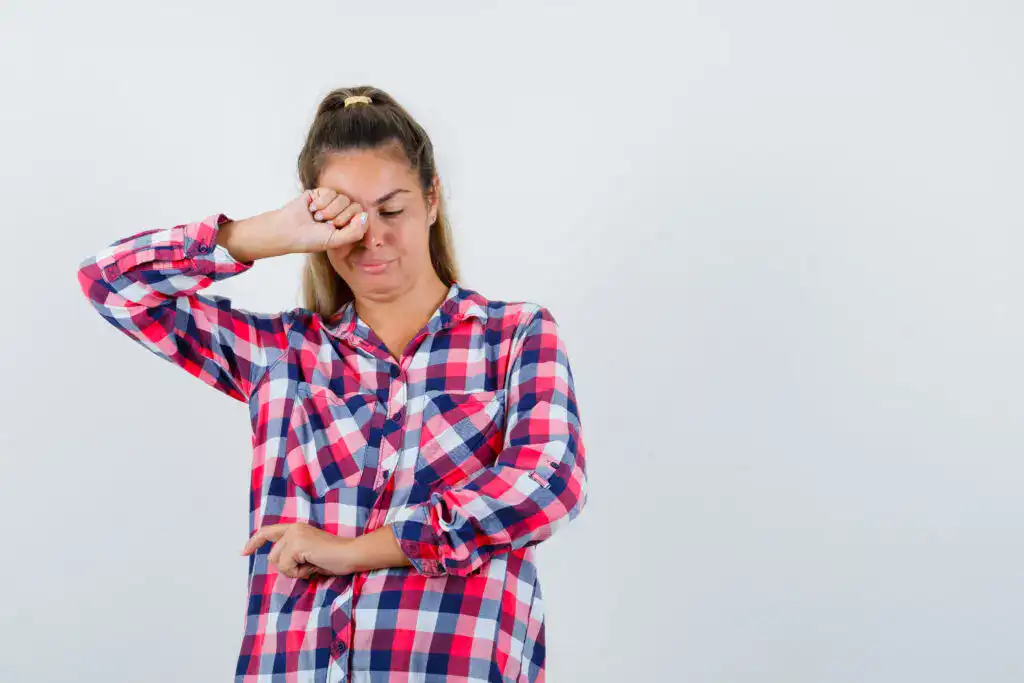 Soñador que muestra fatiga o tristeza, expresión de cansancio emocional o tristeza, en un fondo blanco con camisa a cuadros rojos y azules. – SoyMigrante.com REVISTA