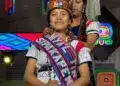 Orgullosa mujer indígena en vestimenta tradicional con banda que dice "Soy Migrante" en evento cultural.