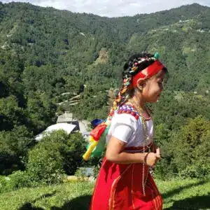 Niña indígena en trajes tradicionales con música y naturaleza en un paisaje montañoso.