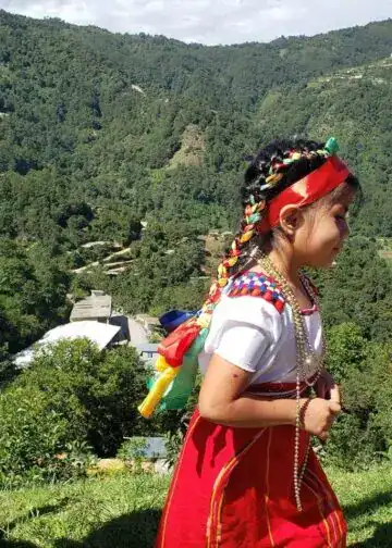 Fotografía Academia de Lenguas Mayas de Guatemala – SoyMigrante.com REVISTA Niña indígena en trajes tradicionales con música y naturaleza en un paisaje montañoso. – SoyMigrante.com REVISTA