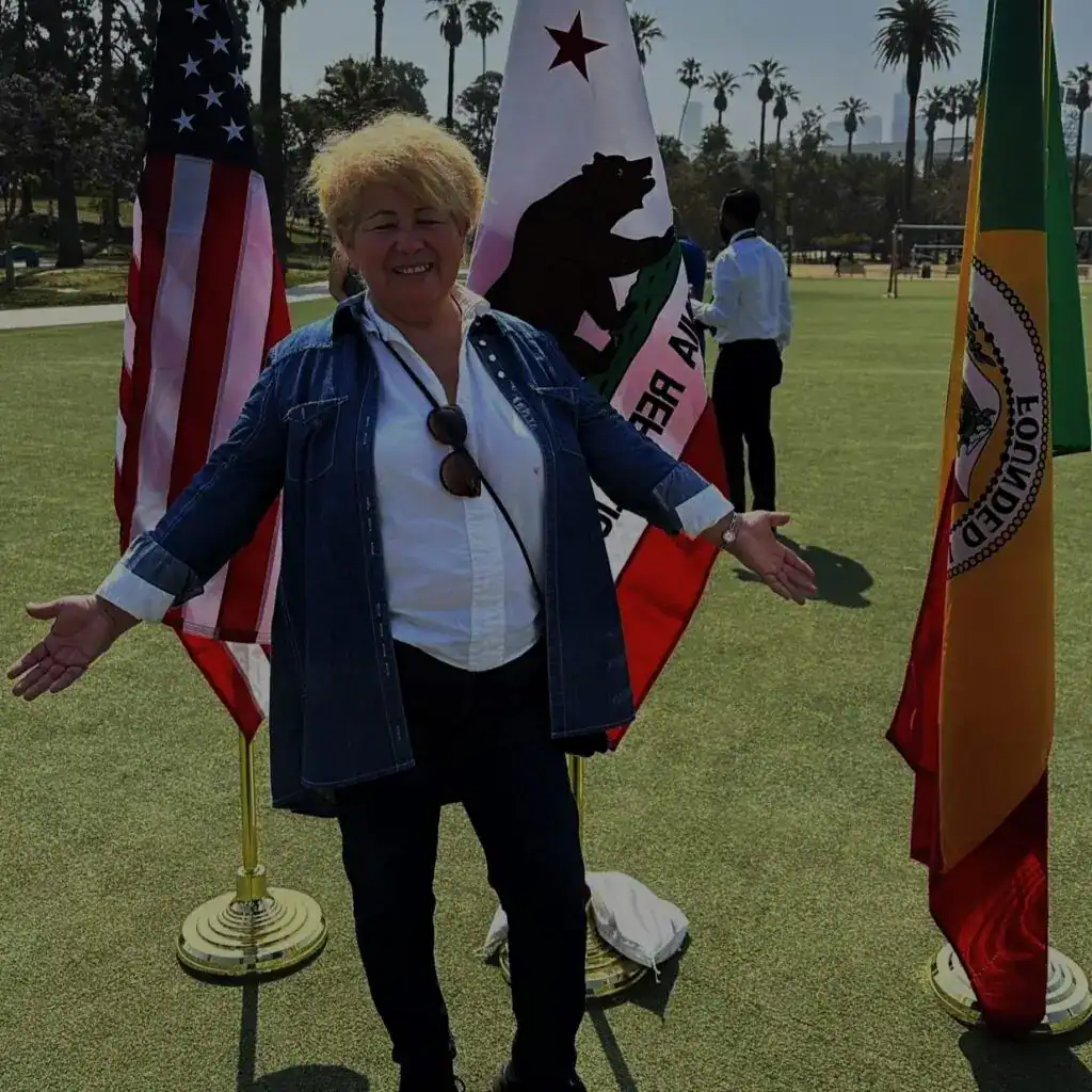 Bandera de Estados Unidos, bandera de California, bandera de Alemania, mujer sonriendo en evento cultural internacional, diversidad y comunidad global. – SoyMigrante.com REVISTA