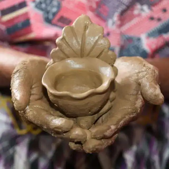 Mano sosteniendo una escultura de barro que representa una taza con una hoja decorativa, símbolo de la cultura y artesanía latinoamericana. – SoyMigrante.com REVISTA