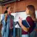 Estudiantes felices celebrando logro académico en aula con certificados y mochila, diversidad cultural, educación y éxito escolar, motivo de orgullo y satisfacción académica.