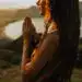 Piel de una mujer con cabello rizado en posición de oración frente a un atardecer, simbolizando paz, esperanza y reflexión, en un entorno natural junto a un río.
