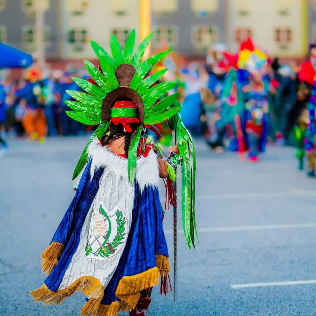 Colorido disfraz tradicional indígena con plumas verdes en desfile cultural en Ciudad, celebración de cultura y migración en la revista SoyMigrante.com REVISTA. – SoyMigrante.com REVISTA