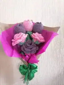 Flores de ganchillo hechas a mano para celebrar el Día de la Madre, en tonos rosa y morado, enmarcadas en papel rosa y verde, ideales para regalos y homenajes a las mamás migrantes.
