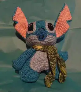 Hecho a mano, peluche crochet de un perro tejida con hilos en colores azul y gris, con orejas grandes color naranja y bufanda tejida en tonos dorados y verdes, ideal para colección o decoración.