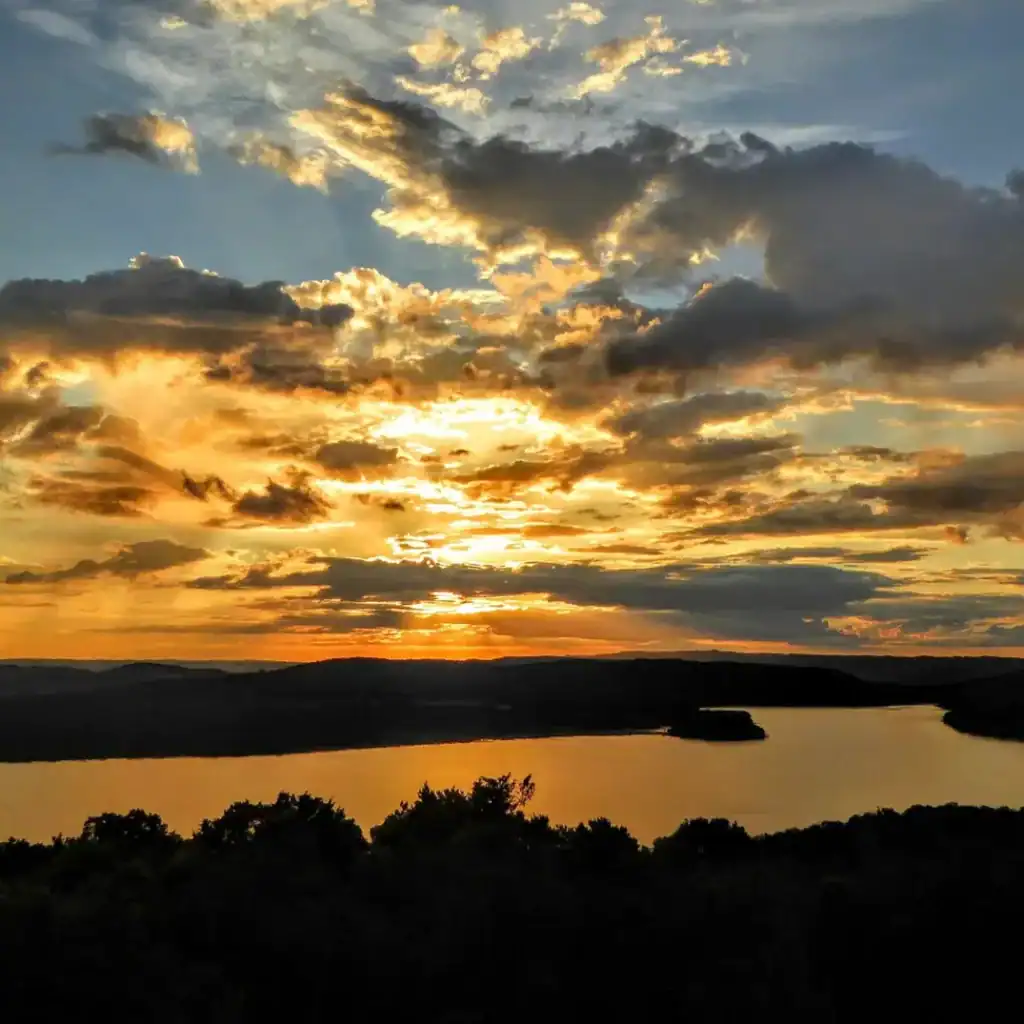 Atardecer en un río con cielo nublado y cálidos tonos dorados, reflejados en el agua, representando la belleza natural y la tranquilidad del paisaje. – SoyMigrante.com REVISTA