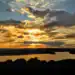 Atardecer en un río con cielo nublado y cálidos tonos dorados, reflejados en el agua, representando la belleza natural y la tranquilidad del paisaje.