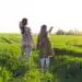 Niña y mujer en campo verde, explorando la naturaleza en un día soleado, promoviendo la conciencia ambiental y la conexión con la tierra.