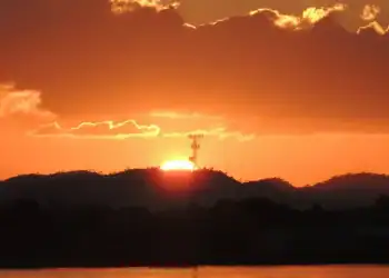 Atardecer en la naturaleza con cielo nublado, sol en el horizonte y reflejo en el agua, simbolizando paz y belleza natural.