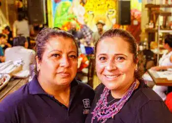 reestaurante ix new york 2 – SoyMigrante.com REVISTA Trabajadoras migrantes en un restaurante latino con decoración colorida y mural de jaguar en el fondo, mostrando la cultura y comunidad migrante en eventos culturales y sociales.