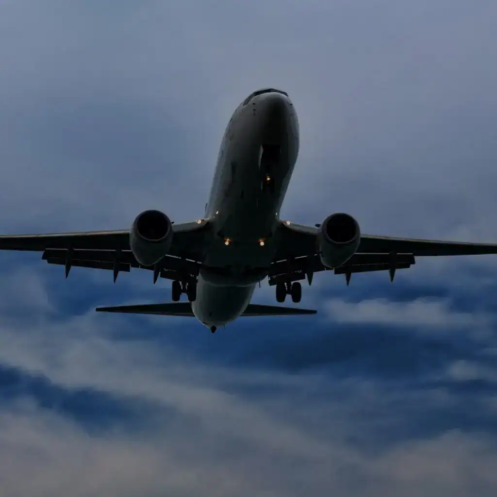 Descending plane to land – SoyMigrante.com REVISTA Avión comercial en vuelo, fotografía tomada desde abajo, cielo nublado, transporte aéreo, aeropuerto, viaje internacional, aerolínea, aeronave moderna, industria aérea, movilidad global. – SoyMigrante.com REVISTA