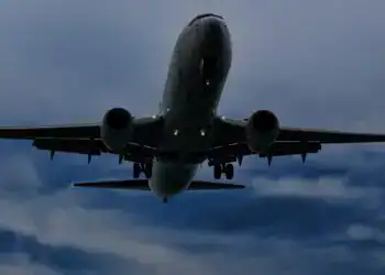 Avión comercial en vuelo, fotografía tomada desde abajo, cielo nublado, transporte aéreo, aeropuerto, viaje internacional, aerolínea, aeronave moderna, industria aérea, movilidad global. – SoyMigrante.com REVISTA
