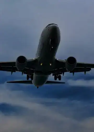 Avión comercial en vuelo, fotografía tomada desde abajo, cielo nublado, transporte aéreo, aeropuerto, viaje internacional, aerolínea, aeronave moderna, industria aérea, movilidad global. – SoyMigrante.com REVISTA