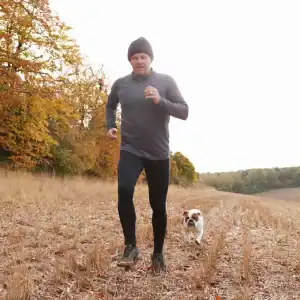 Corredor practicando ejercicio al aire libre, running en campo con perro, salud y bienestar, actividad física en plena naturaleza, promoción del deporte y la vida saludable.