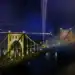 Puente amarillo iluminado en la noche con fuegos artificiales y luces en el fondo, celebración y festividad en el contexto de la revista SoyMigrante.com REVISTA.
