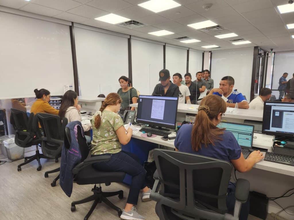 Oficina de atención en el immigrante en un centro de servicios, con personas esperando y personal asistiendo, en un ambiente moderno y eficiente en gestión migratoria. – SoyMigrante.com REVISTA