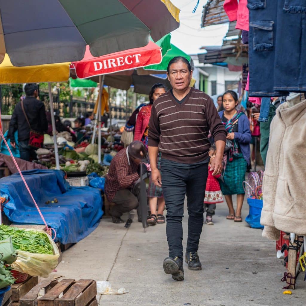Vendedor ambulante en mercado al aire libre en una comunidad latinoamericana, promoviendo cooperación y cultura migrante en espacios públicos.