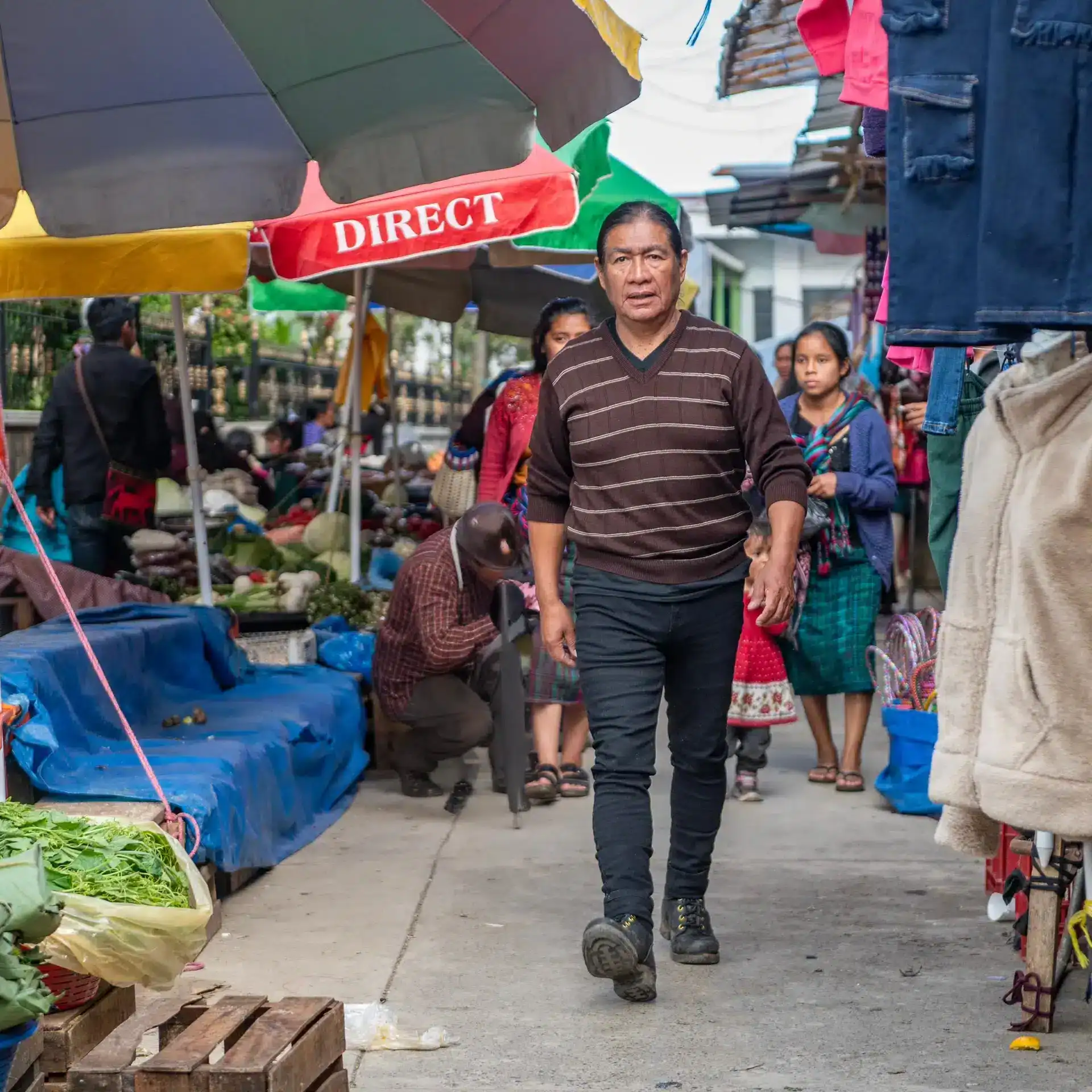 Actor maya q'anjob'al Dionicio Virvez en su pueblo Santa Eulalia Huehuetenango Foto Abel Juárez – SoyMigrante.com REVISTA Vendedor ambulante en mercado al aire libre en una comunidad latinoamericana, promoviendo cooperación y cultura migrante en espacios públicos.