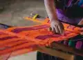Tela de trabajo artesanal con tejido colorido y patrón tradicional, realizada por una mujer indígena en un entorno rural de Latinoamérica.