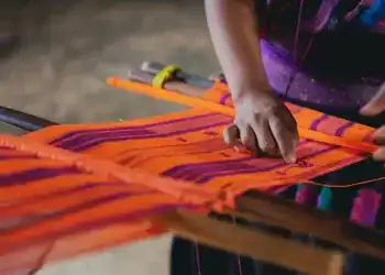 Tela de trabajo artesanal con tejido colorido y patrón tradicional, realizada por una mujer indígena en un entorno rural de Latinoamérica.