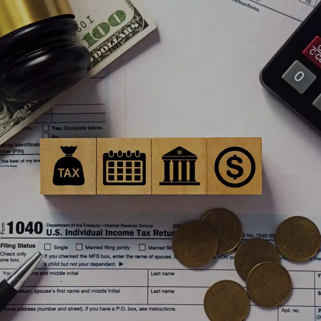 Dinero en efectivo, lápiz y bloques con íconos de impuestos, calendario, banco y dinero, relacionados con la fiscalidad para migrantes y la declaración de impuestos en EE. UU.