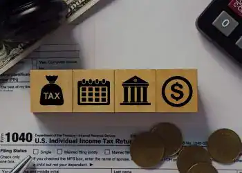 Dinero en efectivo, lápiz y bloques con íconos de impuestos, calendario, banco y dinero, relacionados con la fiscalidad para migrantes y la declaración de impuestos en EE. UU.