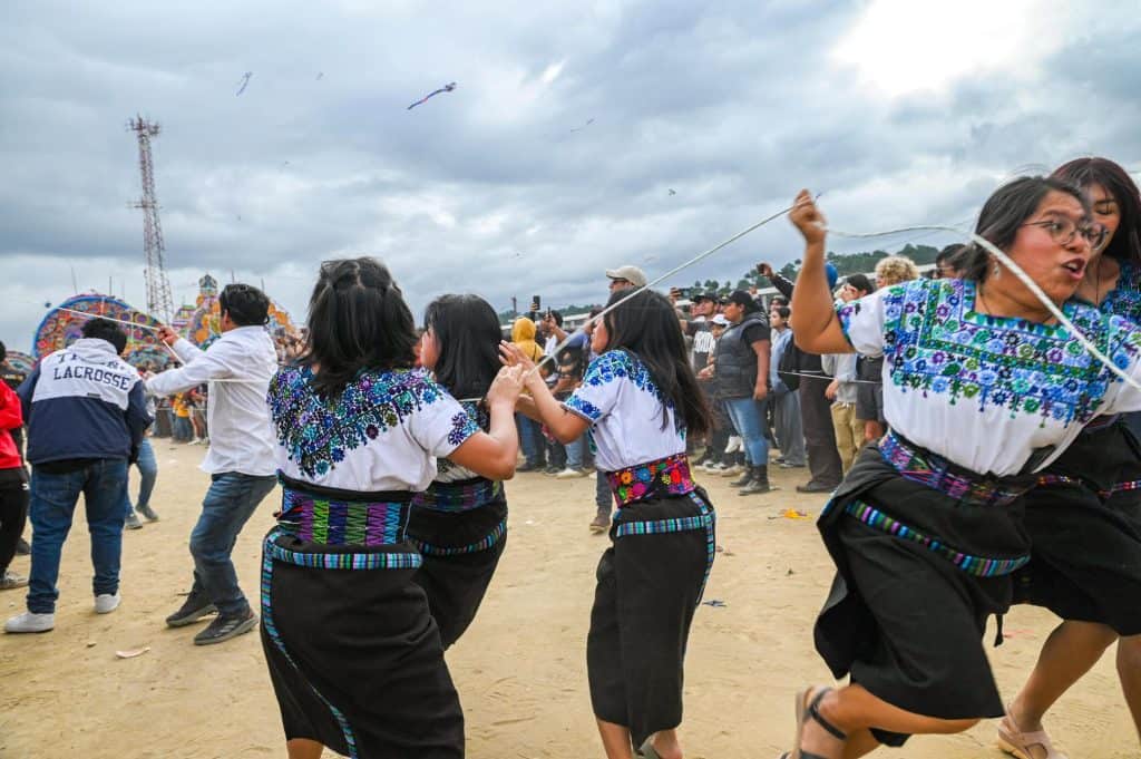 Colaboradores bailando al aire libre en una festividad tradicional, vistiendo ropa típica y rodeados de espectadores en un ambiente festivo y cultural. – SoyMigrante.com REVISTA