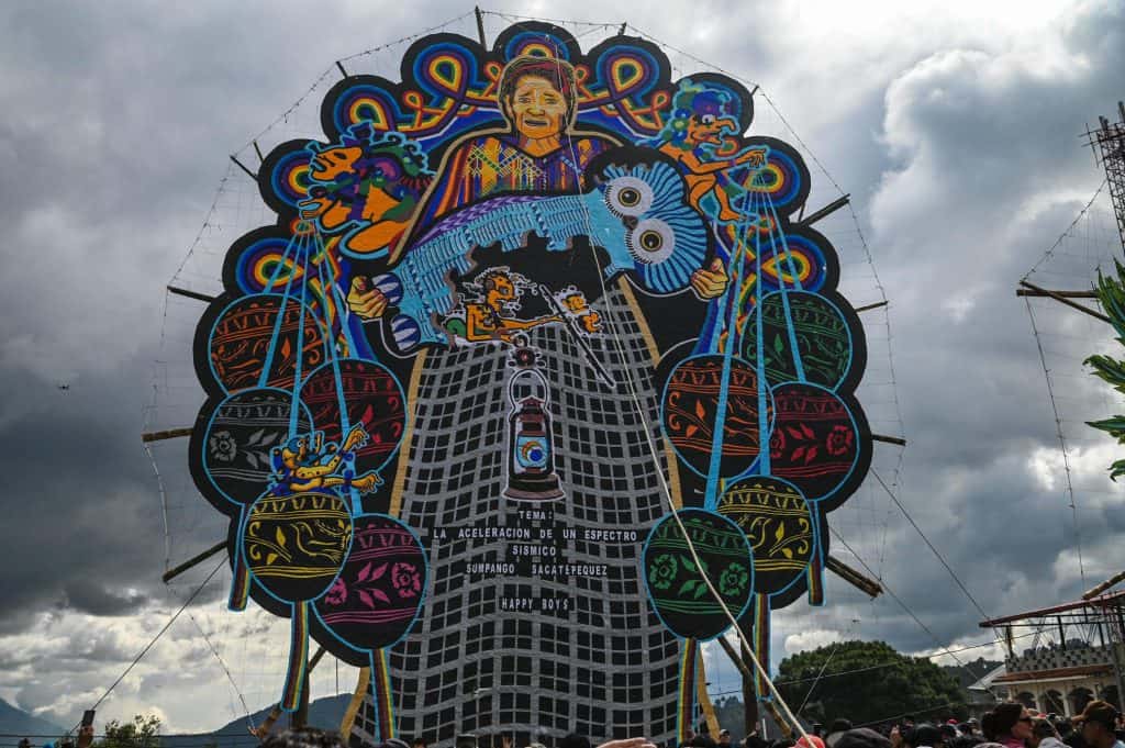 Gigante mural en festival cultural con arte indígena y cultura popular en fondo de cielo nublado, resaltando el valor de las tradiciones y la diversidad cultural en eventos sociales. – SoyMigrante.com REVISTA