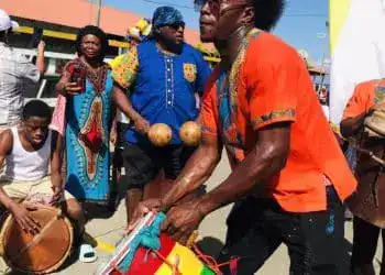 Vibrante celebración cultural con artistas tocando tambores y bailando en una festividad tradicional africana, destacando la música, el baile y las vestimentas coloridas.