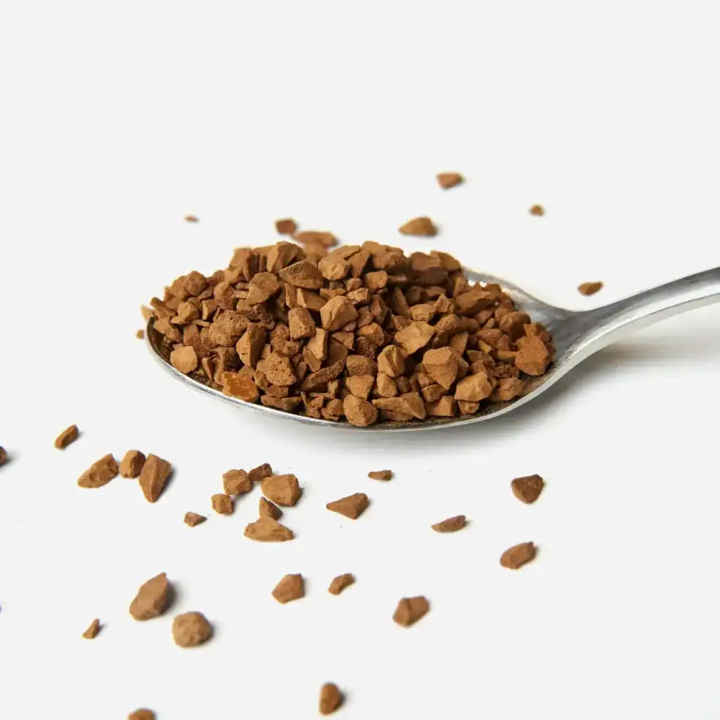 Polvo de café soluble en una cuchara, enfoque en granulado de café instantáneo, fondo blanco. Ideal para artículos sobre cultura migrante, alimentación y estilo de vida en la revista SoyMigrante.com. – SoyMigrante.com REVISTA