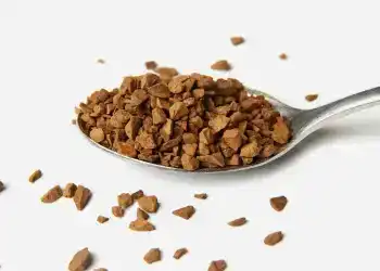 Inventos guatemaltecos que dejaron huella en la historia 1 – SoyMigrante.com REVISTA Polvo de café soluble en una cuchara, enfoque en granulado de café instantáneo, fondo blanco. Ideal para artículos sobre cultura migrante, alimentación y estilo de vida en la revista SoyMigrante.com.