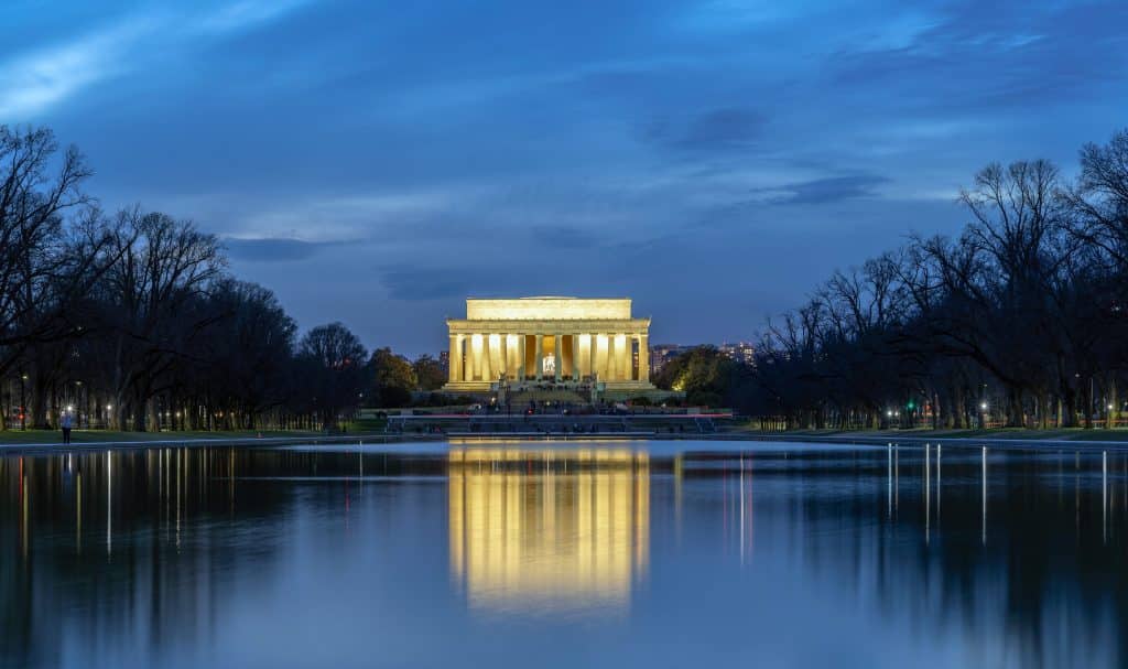 Impresión nocturna del Monumento a Lincoln en Washington D.C., iluminado en un cielo azul y reflejado en el agua del Reflecting Pool, destacando como símbolo de historia y libertad en Estados Unidos.