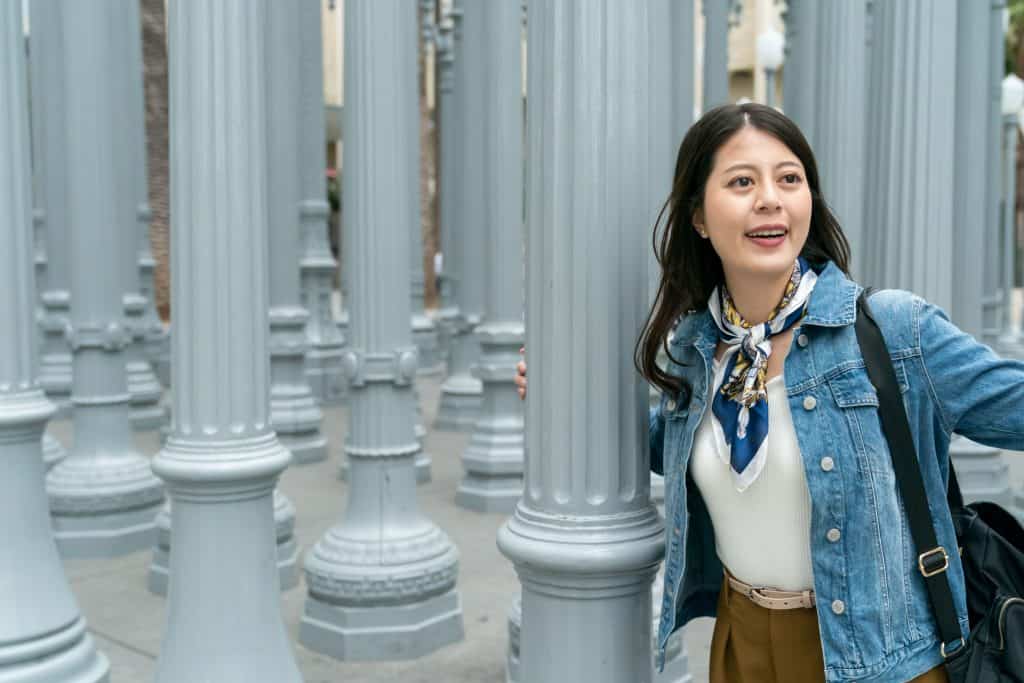 Joven mujer explorando columnas en ciudad, imagen para revista SoyMigrante.com, sobre migrantes y experiencias de vida, con enfoque en comunidad y cultura migrante.