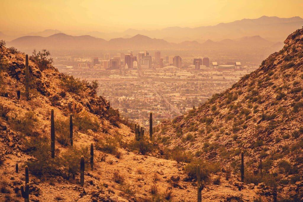 Paisaje del desierto de Arizona con cactus saguaro y vista panorámica de la ciudad de Phoenix al fondo, en un atardecer dorado, ideal para contenido sobre migrantes, cultura y vida en Arizona. – SoyMigrante.com REVISTA