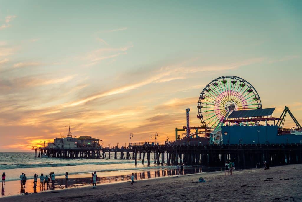 Paseo por el muelle de Santa Mónica al atardecer, con la rueda de la fortuna iluminada, familia disfrutando en la playa, un icono de Los Ángeles, California, atractivo turístico y cultural en Estados Unidos.