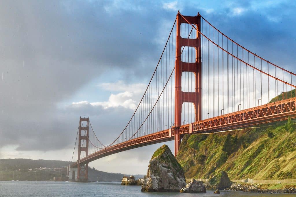 Puente Golden Gate en San Francisco, símbolo de California y atracción turística mundial. Foto icónica en tonos rojos y cielo nublado, representando infraestructura y belleza arquitectónica.