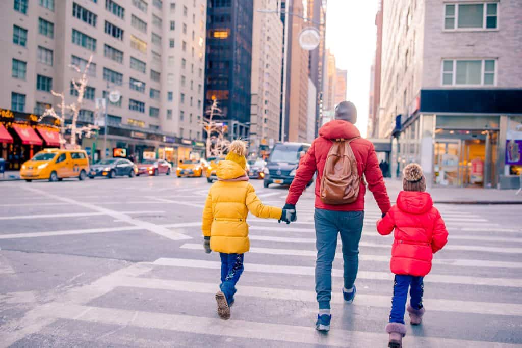 Pasajero con niños cruzando la calle en ciudad cosmopolita, foco en diversidad y vida urbana en una imagen vibrante y moderna.