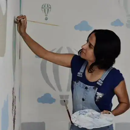 Pintora muralista adolescente creando arte en la pared con aerógrafo en un mural colorido con nubes y globo aerostático, promoviendo cultura y arte en la comunidad. – SoyMigrante.com REVISTA