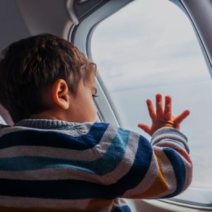 Niño mirando por la ventana de un avión, simbolizando viajes y migración, en el contexto de la revista SoyMigrante.com Revoluciona tus perspectivas sobre migración y cultura con contenido inspirador y relevante.