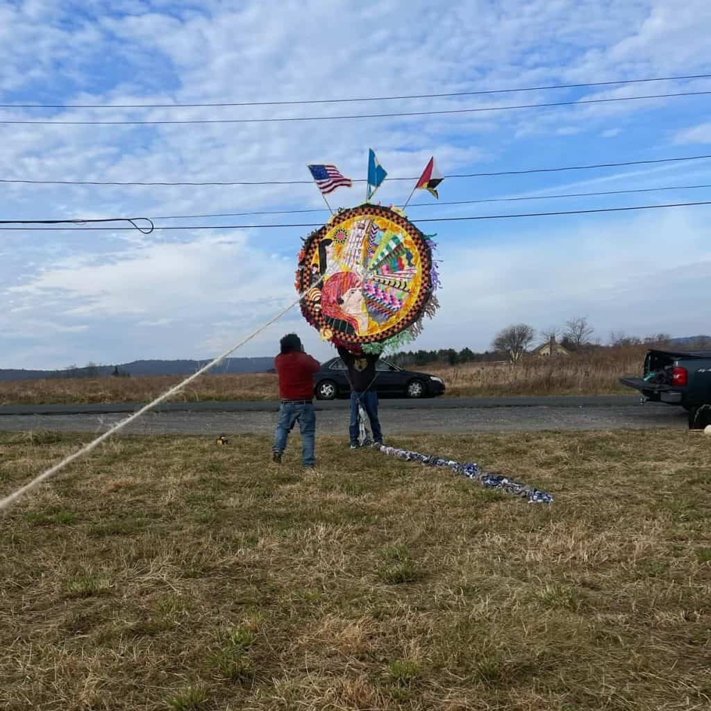 Colorida ofrenda de Día de Muertos en un campo abierto, con banderas de Estados Unidos, México y Guatemala; celebrando cultura y tradiciones migrantes. – SoyMigrante.com REVISTA