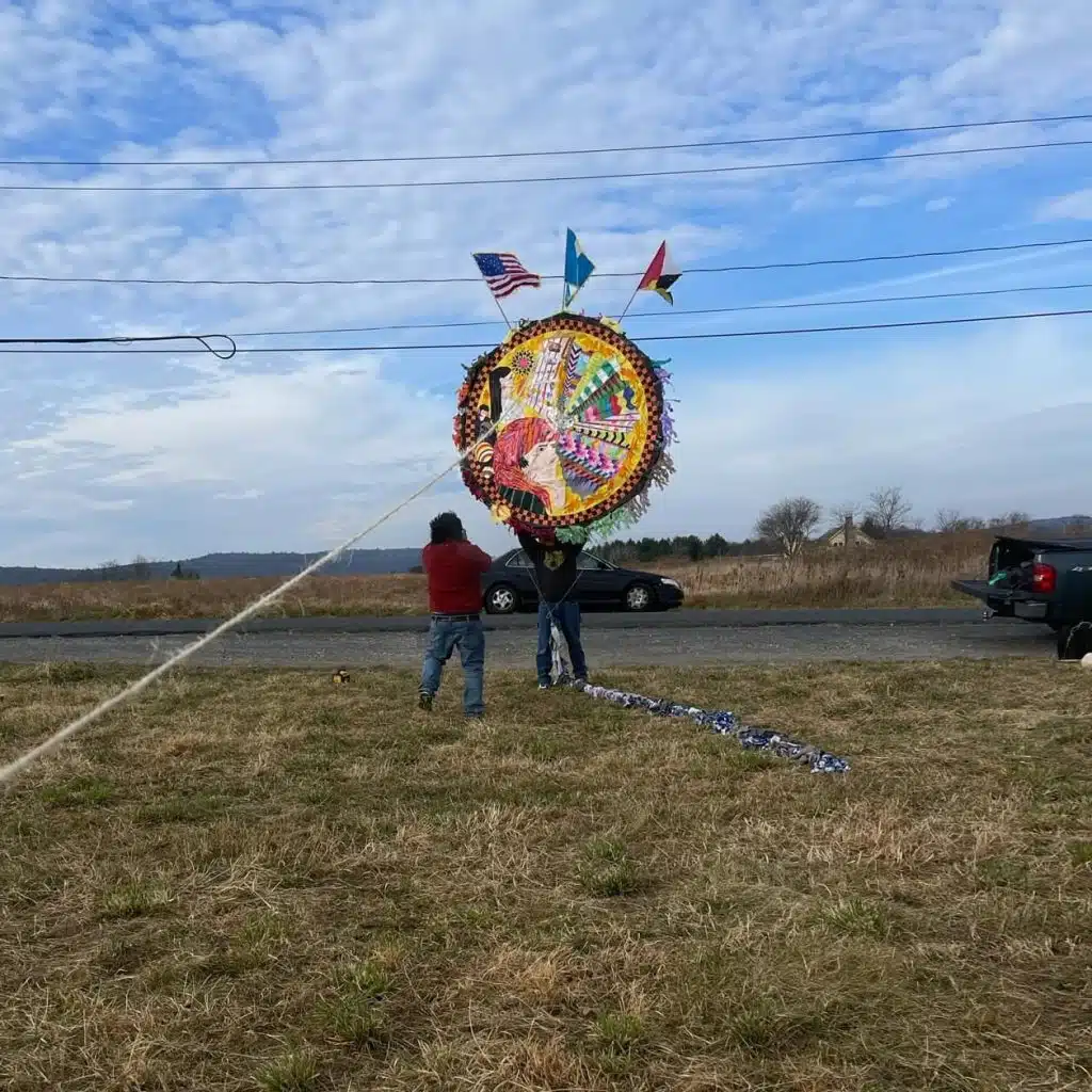Colorida ofrenda de Día de Muertos en un campo abierto, con banderas de Estados Unidos, México y Guatemala; celebrando cultura y tradiciones migrantes.